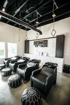 an empty room with black leather chairs and ottomans in the center, along with white brick walls