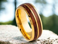 a gold ring with wood inlays on top of a rock, near some trees