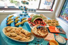 a blue table topped with lots of desserts and pastries next to a window