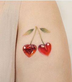 two heart shaped cherries on the back of a woman's arm with leaves