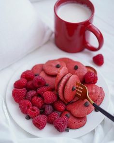 a white plate topped with raspberries and cookies next to a cup of coffee