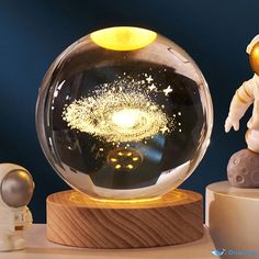 an astronaut figurine next to a glass ball with fireworks in it on a table