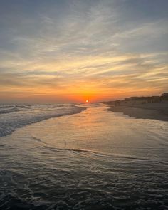 the sun is setting over the water at the beach with waves coming in to shore