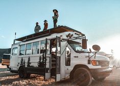 two people standing on top of a bus in the middle of a field with other vehicles