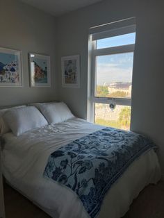 a bed sitting under a window in a bedroom next to two pictures on the wall