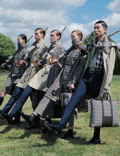 a group of people dressed in plaid outfits carrying suitcases and walking through the grass