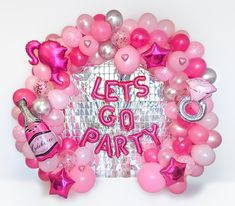 a pink and silver party wreath with balloons, confetti, wine bottles and other items