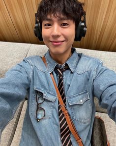 a young man wearing headphones and a tie sitting on a couch with his hands in the air