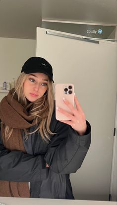 a woman taking a selfie in front of a mirror wearing a hat and scarf