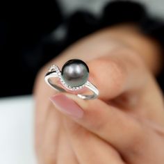 a woman's hand holding a ring with a black pearl and diamonds on it