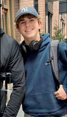 a young man wearing headphones standing in front of a brick building with his arms around him