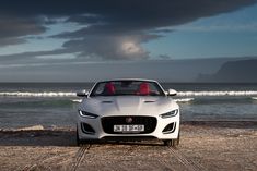 a white sports car is parked on the beach by the ocean with dark clouds in the background