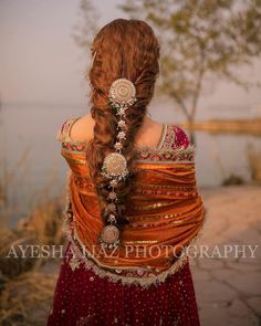 a woman with long red hair wearing an orange and gold dress, braided into a ponytail