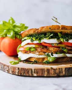 a sandwich with tomatoes and lettuce on a cutting board next to some basil