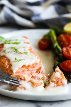 a white plate topped with salmon and veggies next to a knife and fork