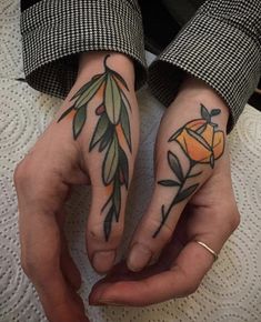 two people with tattoos on their hands holding each other's fingers, one has an orange and the other has green leaves