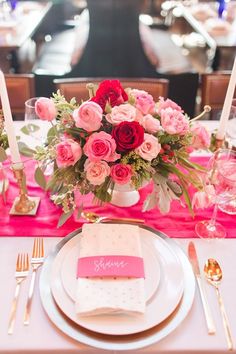 a table set with pink and red flowers, silverware and napkins on it