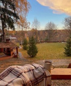 a coffee cup sitting on top of a wooden table next to a forest filled with trees