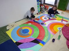 two children are sitting on the floor working on an art project with colorful circles painted on it