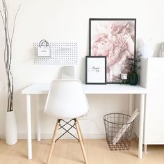 a white desk topped with a computer monitor next to a vase filled with pink flowers