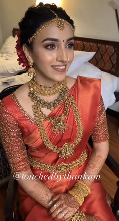 a woman in an orange sari with gold jewelry on her neck and hands clasped