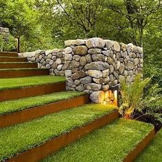 a stone wall with grass growing on the side and steps leading up to it in front of trees