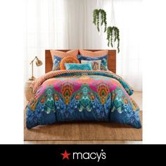 a bed with colorful comforters and pillows on top of it in a room next to a potted plant