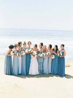 a group of women standing next to each other on top of a sandy beach near the ocean