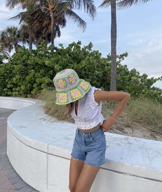 a woman leaning against a wall wearing a hat and denim shorts with crocheted flowers on it