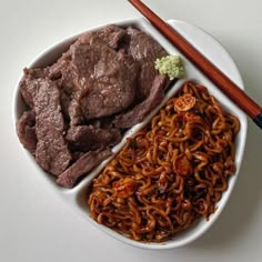 a white plate topped with meat and noodles next to chopsticks