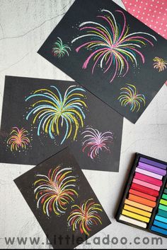 three black cards with colored fireworks on them next to markers and crayon pens