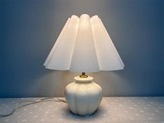 a white table lamp sitting on top of a bed next to a night stand and wall