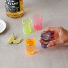 a person holding a shot glass in front of four different colored cups on a table