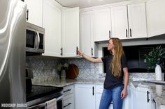 a woman standing in a kitchen pointing at the microwave