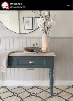 a table with flowers in a vase on top of it and a mirror above it