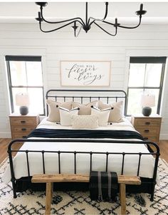 a bedroom with white walls and black iron bed frame, two nightstands, and a bench in front of the bed