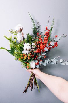 a person holding a bunch of flowers with red berries and greenery on it's stems