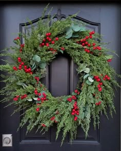 a wreath is hanging on the front door with red berries and greenery around it