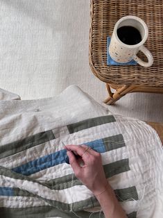 a person is sewing on a quilt next to a basket and cup of espresso