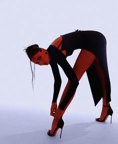 a woman in black and red is bending over with her foot on the ground while wearing high heels