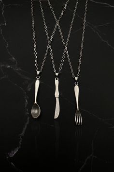 three forks and spoons hanging from chains on a black surface with a marble background