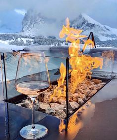 a glass of wine sitting on top of a table next to a fire in the fireplace