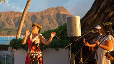 two women are performing on stage in front of the ocean with mountains in the background