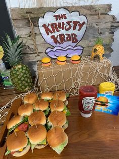 a table topped with lots of sandwiches next to pineapples and ketchup