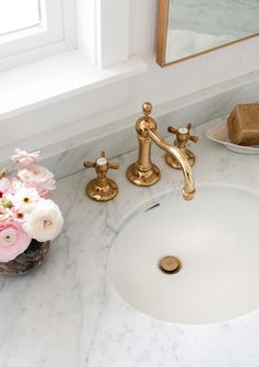 a bathroom sink with gold faucet and marble counter top next to a window