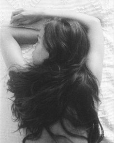 a black and white photo of a woman laying on a bed with her hair blowing in the wind