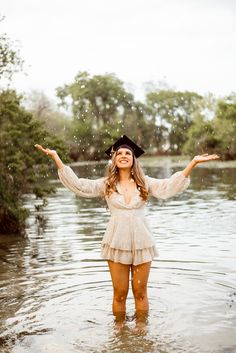 a woman standing in the water with her arms spread out and wearing a hat on top