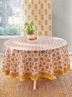 an orange and white table cloth on top of a round table in front of a window