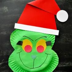 a paper plate with a green face wearing a santa's hat on top of it