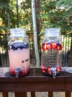 two mason jars with strawberries and blueberries in them sitting on a wooden table